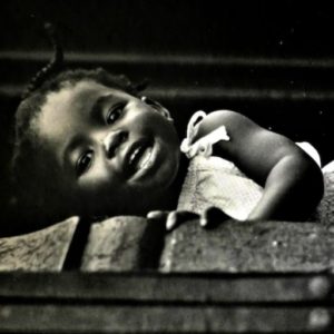 Black and White photo of little African American girl laying on wall